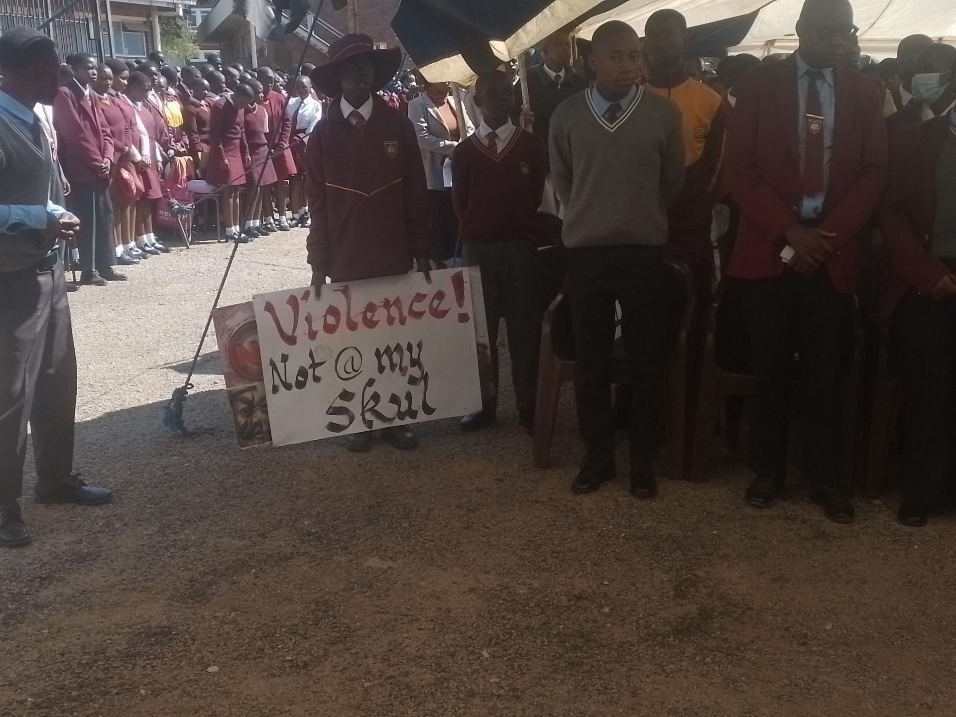 Students holding a 'Violence! Not @ my Skul' placard at a school assembly